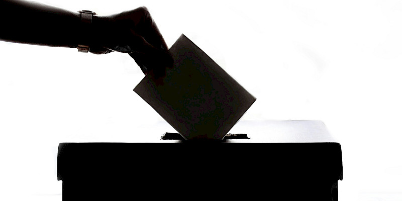 Auf dem schwarz-weiß Bild ist eine Hand zu sehen, die ihren Wahlzettel in eine Wahlurne steckt.