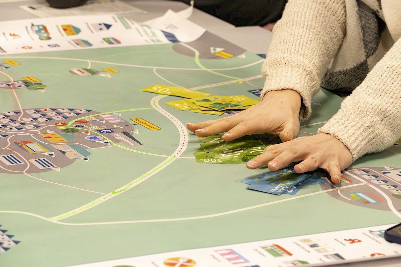 Das ist Mobiland: Das Bild zeigt die Spielfläche, auf der Straßen und Radverbindungen eingezeichnet sind. Zwei Hände greifen zu Spielgeld. Foto: Franke/LNVG
