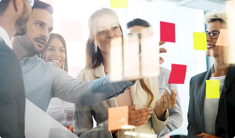 Workshop: Teilnehmerinnen und Teilnehmer stehen hinter einer transparenten Wand mit Klebezetteln.