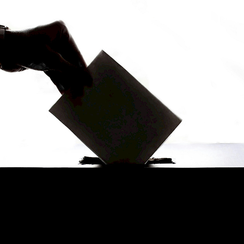 Auf dem schwarz-weiß Bild ist eine Hand zu sehen, die ihren Wahlzettel in eine Wahlurne steckt.