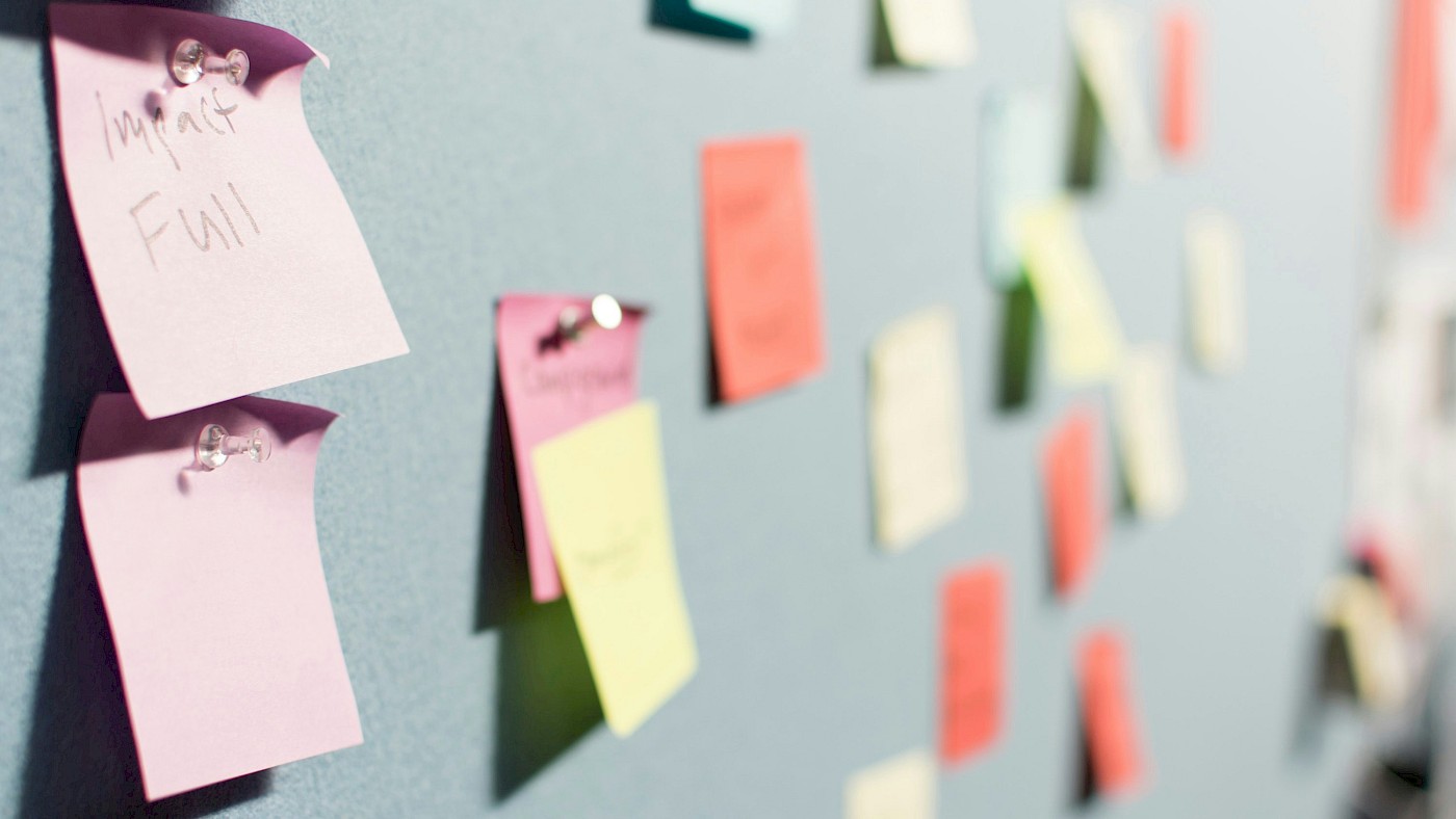 Auf dem Bild sind bunte Post-Its zu sehen, die an Stellwänden sind.