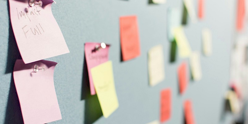 Auf dem Bild sind bunte Post-Its zu sehen, die an Stellwänden sind.