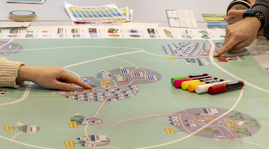 Zwei Hände zeigen auf den Spielplan des Planspiels.